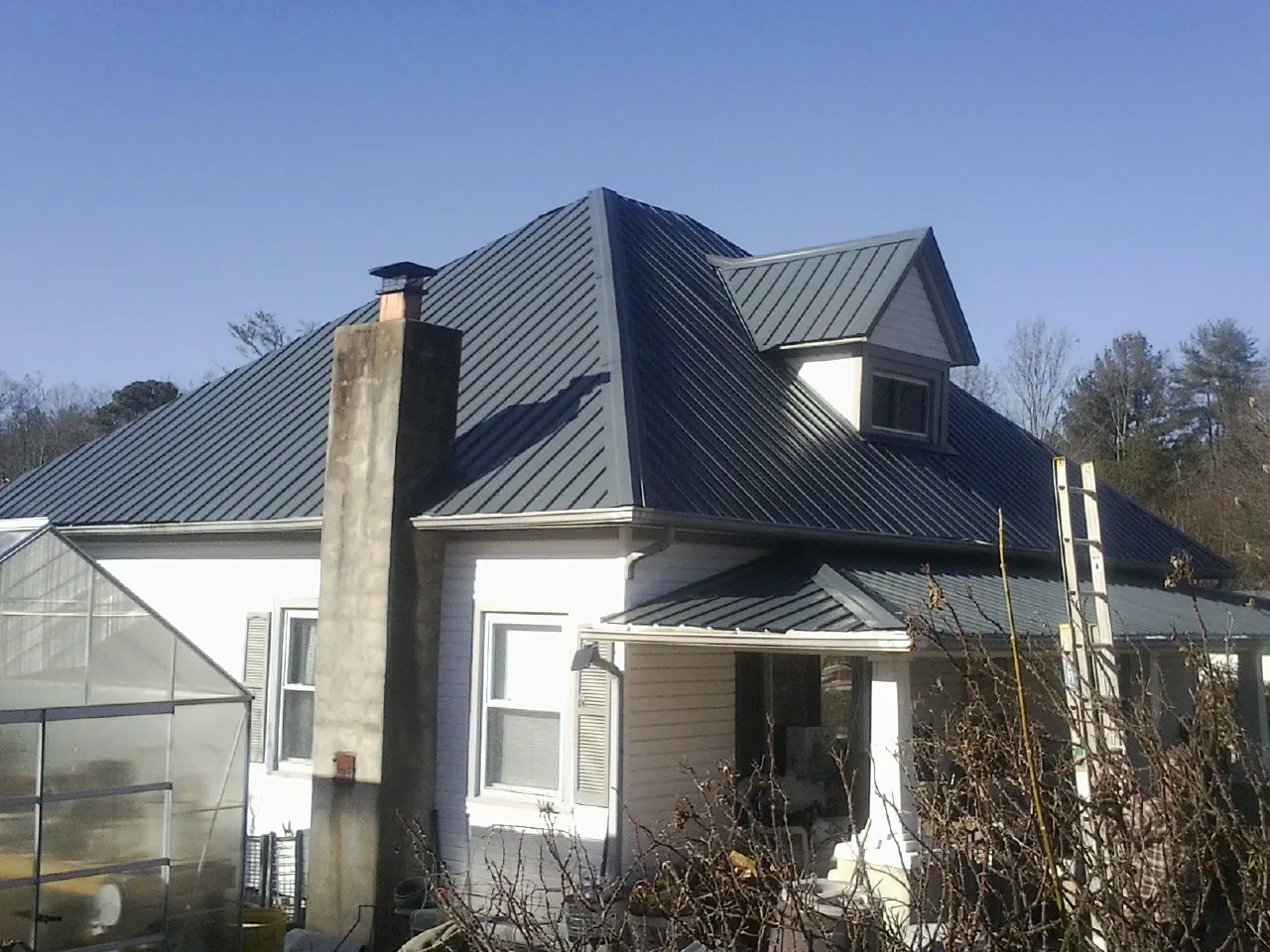 Dark blue standing seam metal roof on a white farmhouse with dormer — Slate & Tile Roof Repair by Roofing Brothers in Cartwright