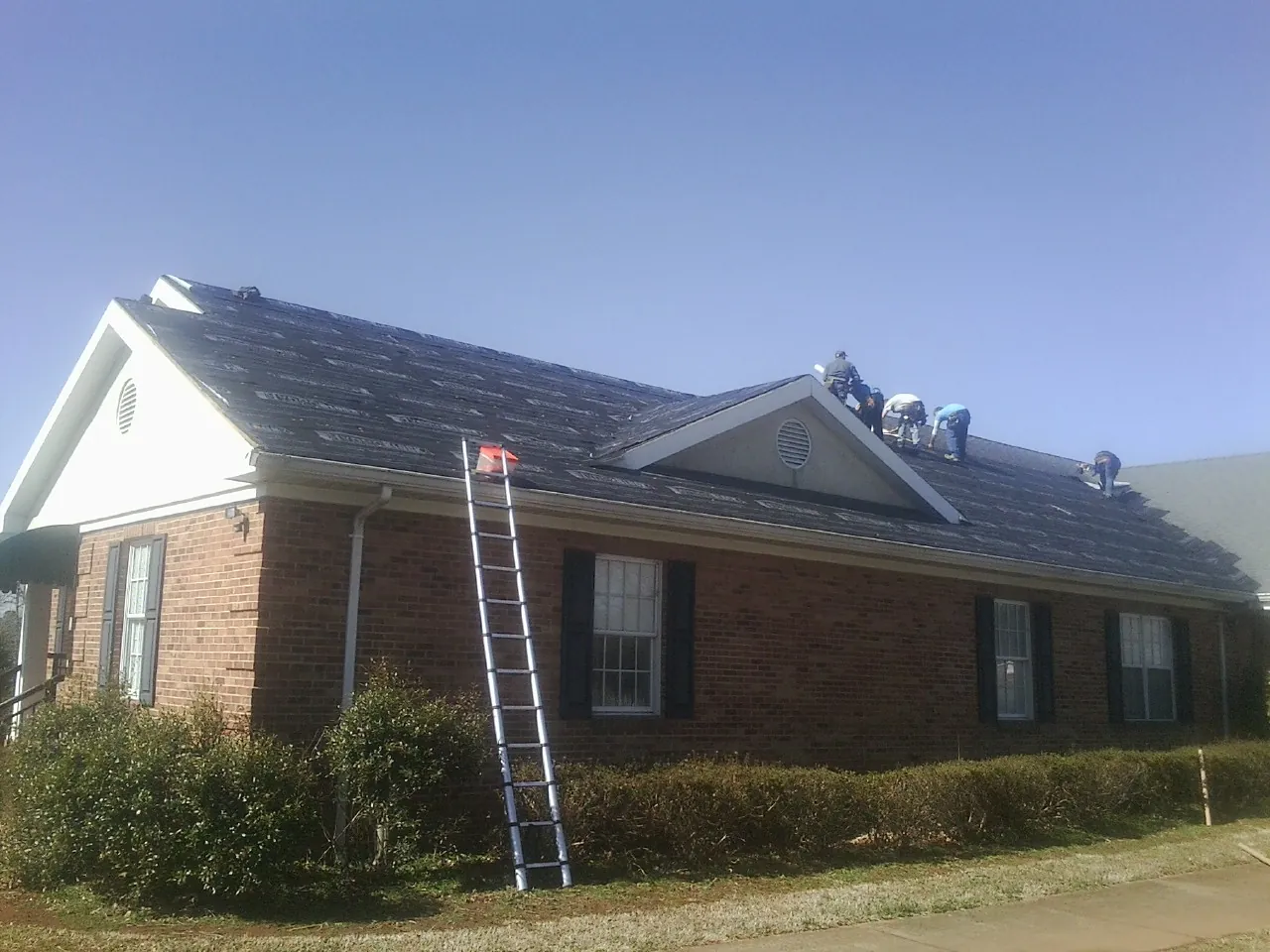 Crew tearing shingles off a brick ranch roof with a ladder set — Emergency Roof Repair work by our crew in Cartwright