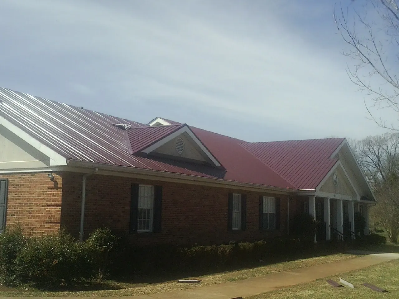 Red metal roof with gabled entries on a long brick building, from a Hail Damage Roof Repair job in Cartwright