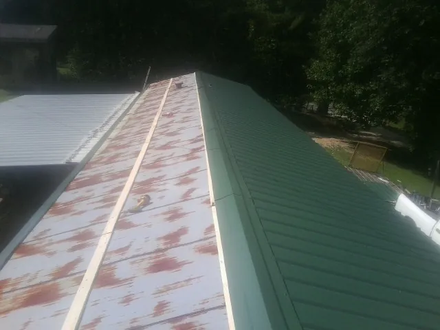 Old rusted panels beside newly installed green metal roofing — Wind Damage Roof Repair by Roofing Brothers in Cartwright